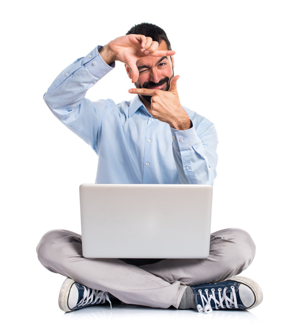 Ein Mann mit blauem Hemd sitzt mit verschränkten Beinen und einem Laptop auf dem Schoß und formt mit seinen Händen einen Rahmen vor seinem Gesicht, während er lächelt.